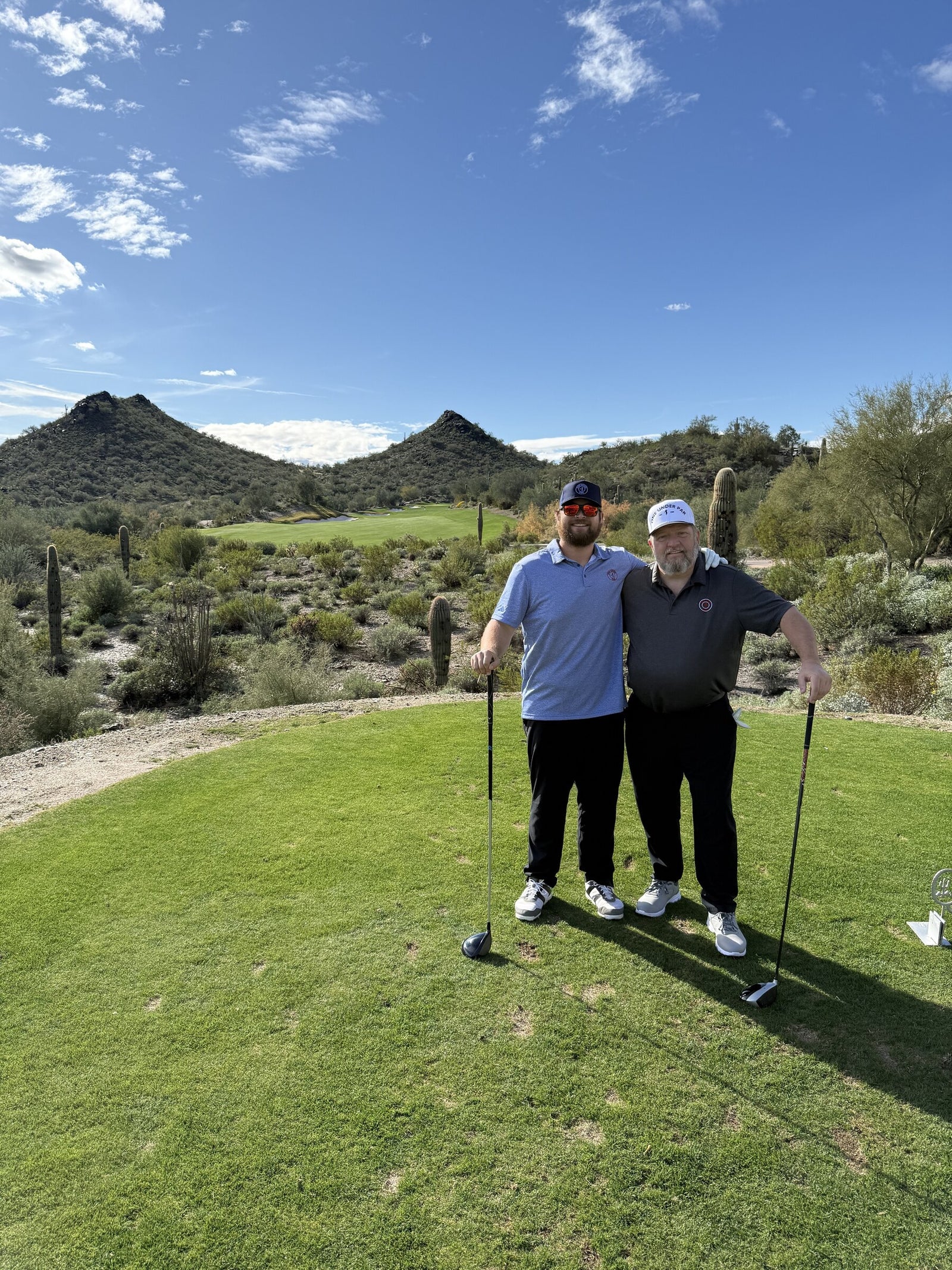 Two golfers wearing One Under Par hats together at Quintero Golf Club