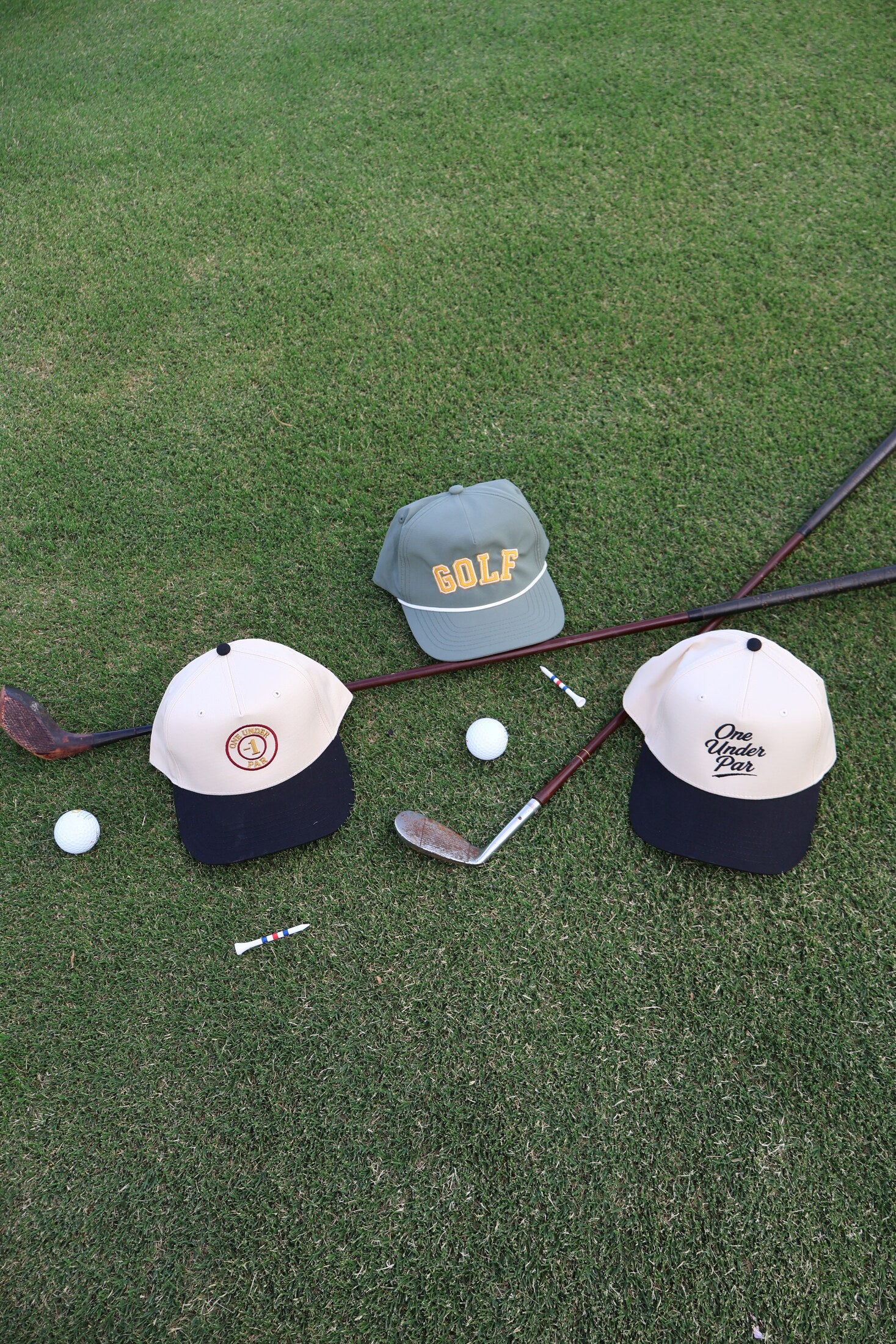One Under Par golf hats arranged on grass with vintage golf clubs
